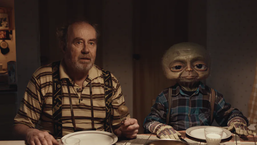 En man vid köksbordet bredvid utomjordingen Roland i Arne Goes to Space